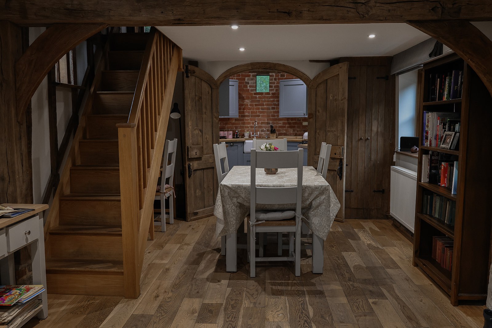 The dining table at The Oast, with timber stairs to the left and the round brick kitchen through the open arch