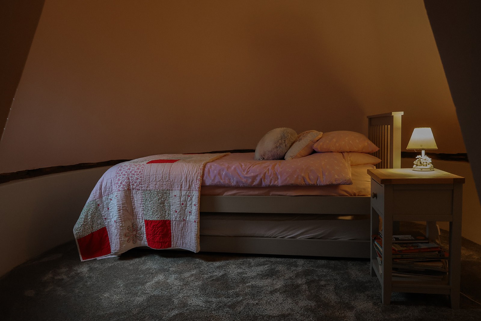 The single bed in the round bedroom at The Oast, with its pull-out truckle stored underneath and a lamp on the bedside table