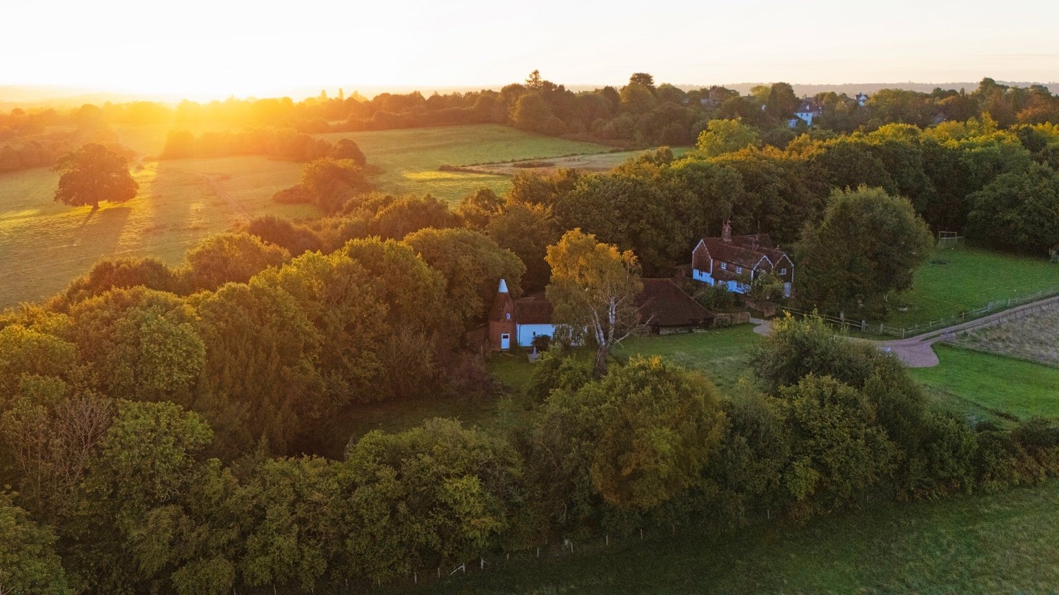 A sunset aerial view of Martins Farm, with The Oast and farmhouse among trees and the surrounding High Weald fields beyond