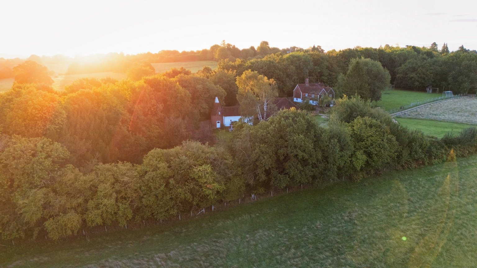 A closer aerial view of Martins Farm at sunset, with trees around the buildings and a green field in the foreground