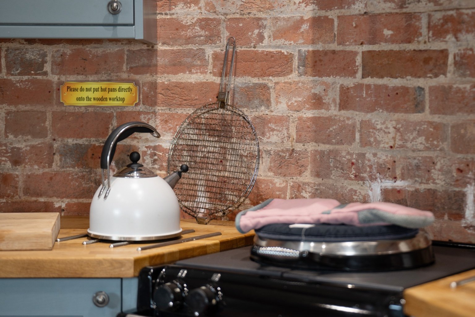 A white kettle on the black AGA beside exposed brickwork and a wooden worktop at The Oast