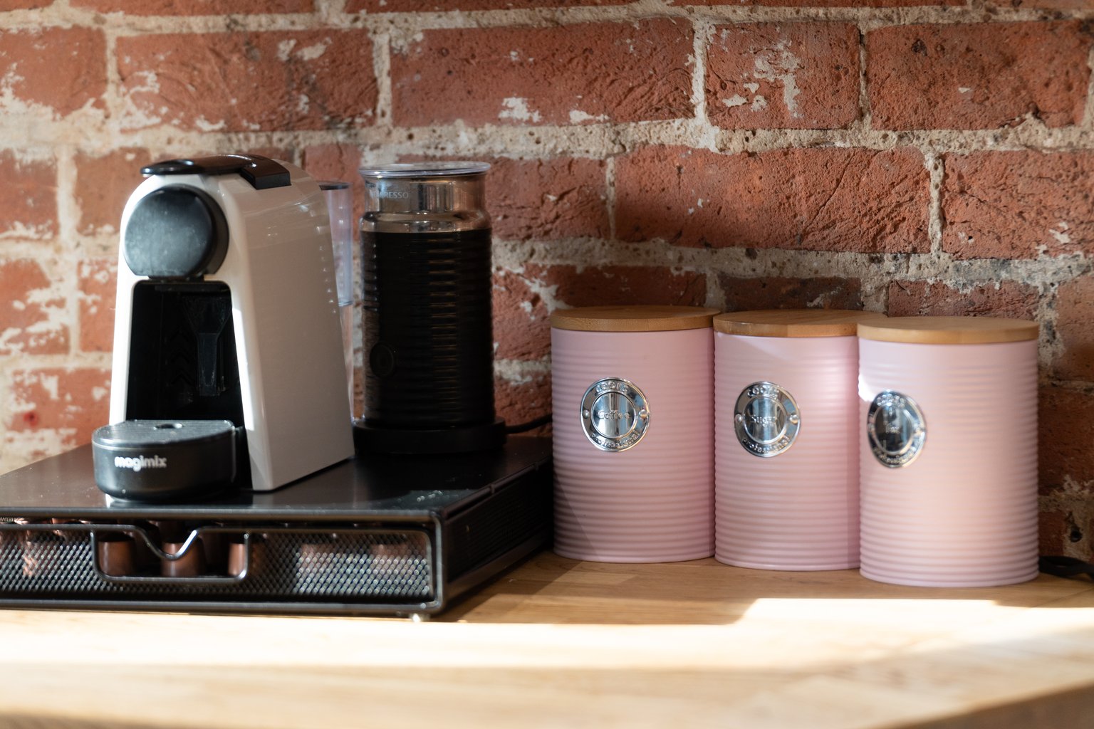 The coffee machine, milk frother and pink storage tins on the kitchen worktop at The Oast