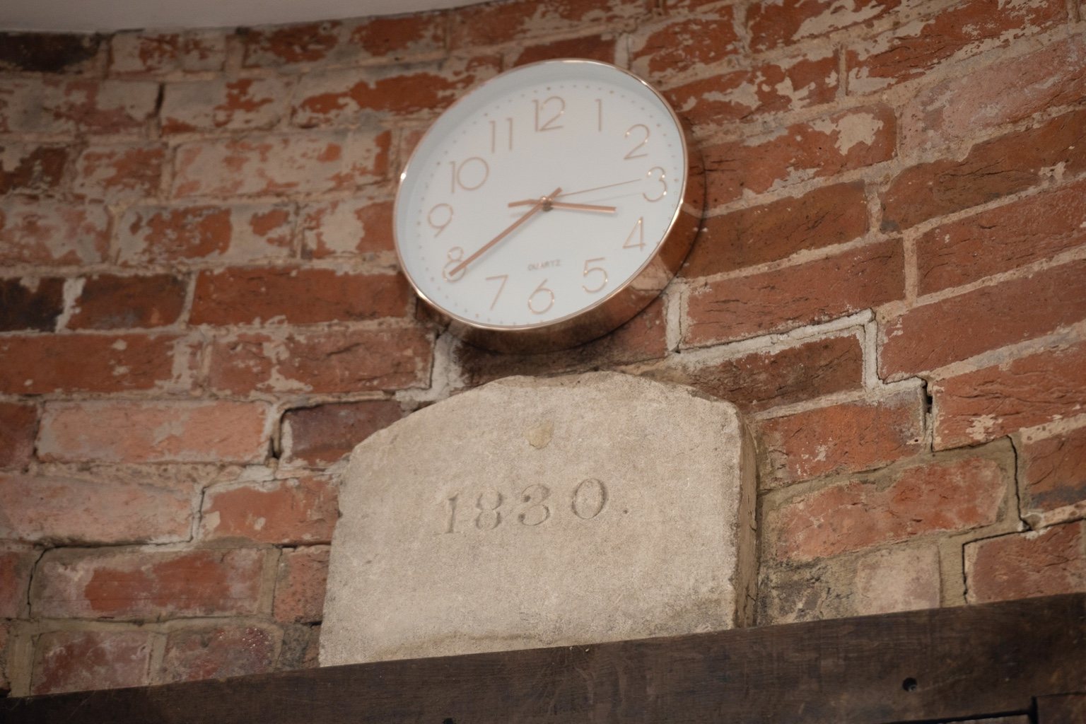 A stone inscribed 1830 above a timber lintel in the brick wall at The Oast, with a clock above it