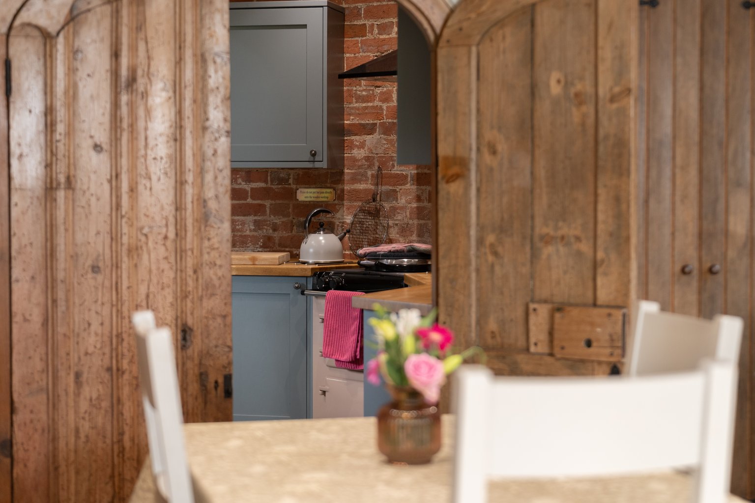 Looking past the dining table and open timber doors to the AGA in the round kitchen at The Oast