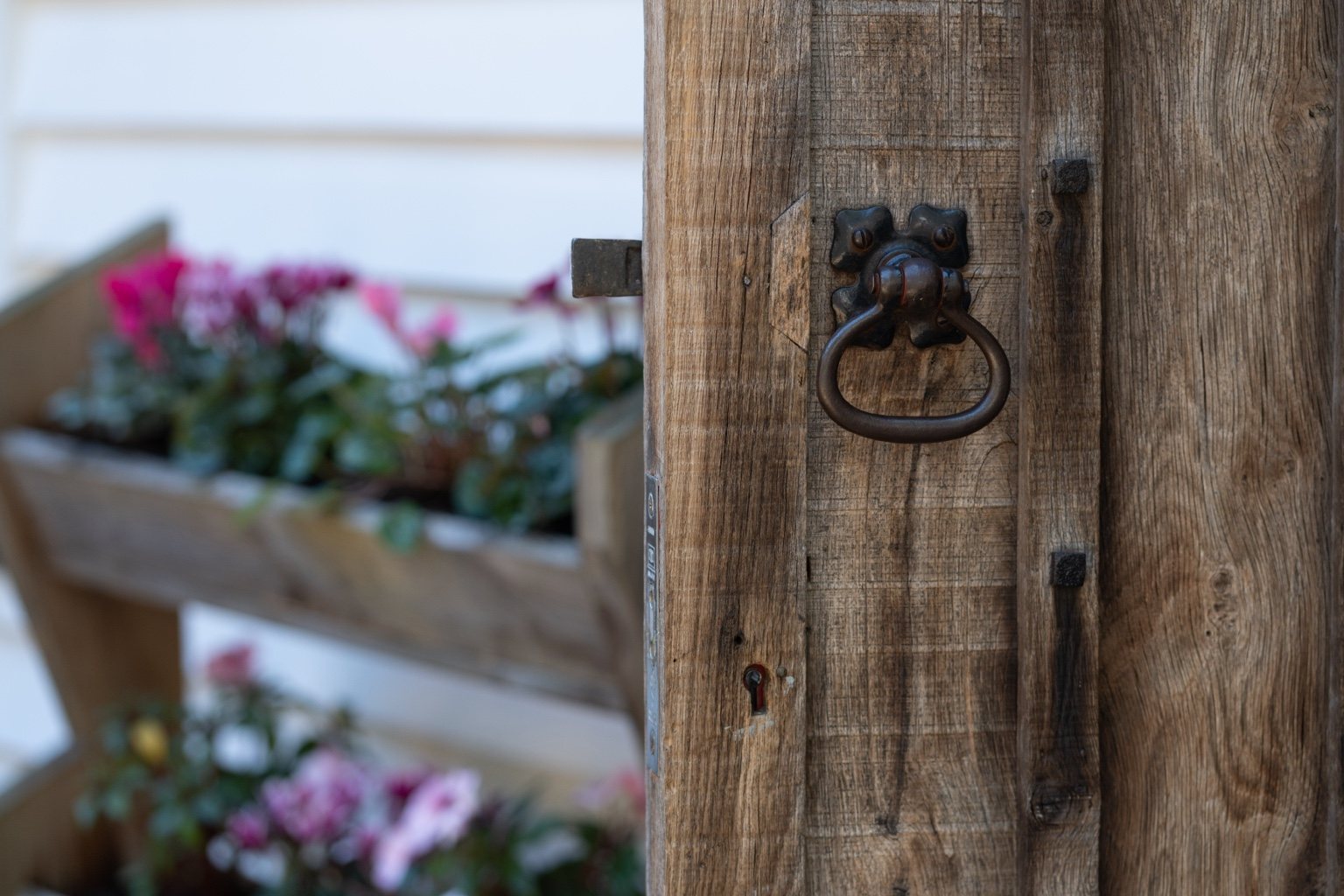 The timber entrance door at The Oast, with an iron ring handle and pink flowers beside the doorway