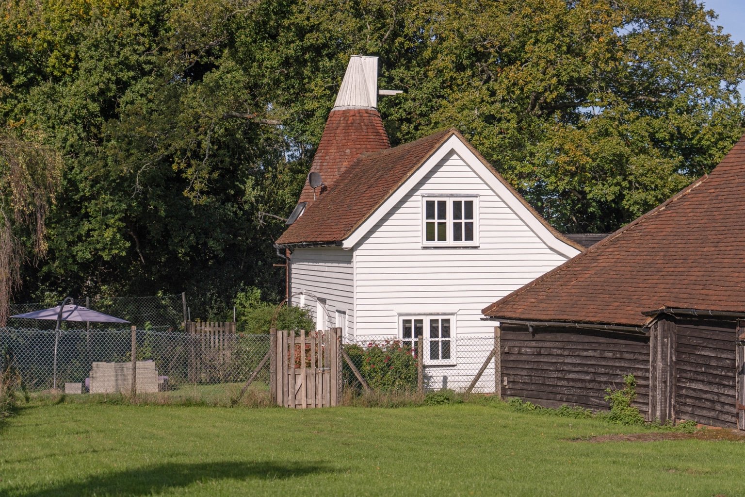 The white weatherboarded Oast and its tiled kiln roof, seen from the lawn beside the barn
