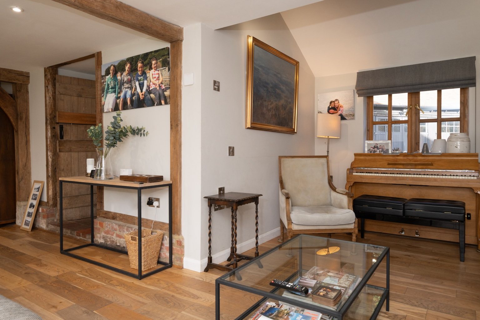 The piano corner in the sitting room at The Oast, with an armchair, exposed timbers and a glass coffee table