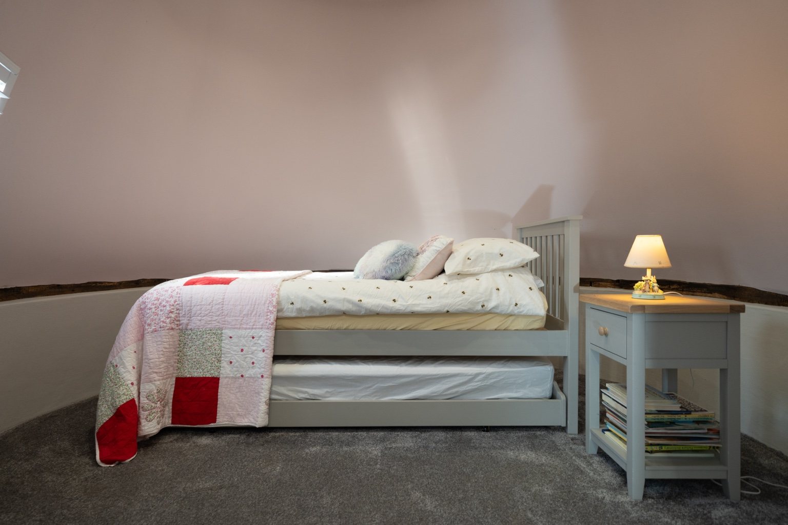 The second bedroom at The Oast, with a single bed, a pull-out bed stored underneath, a patchwork quilt and a bedside table