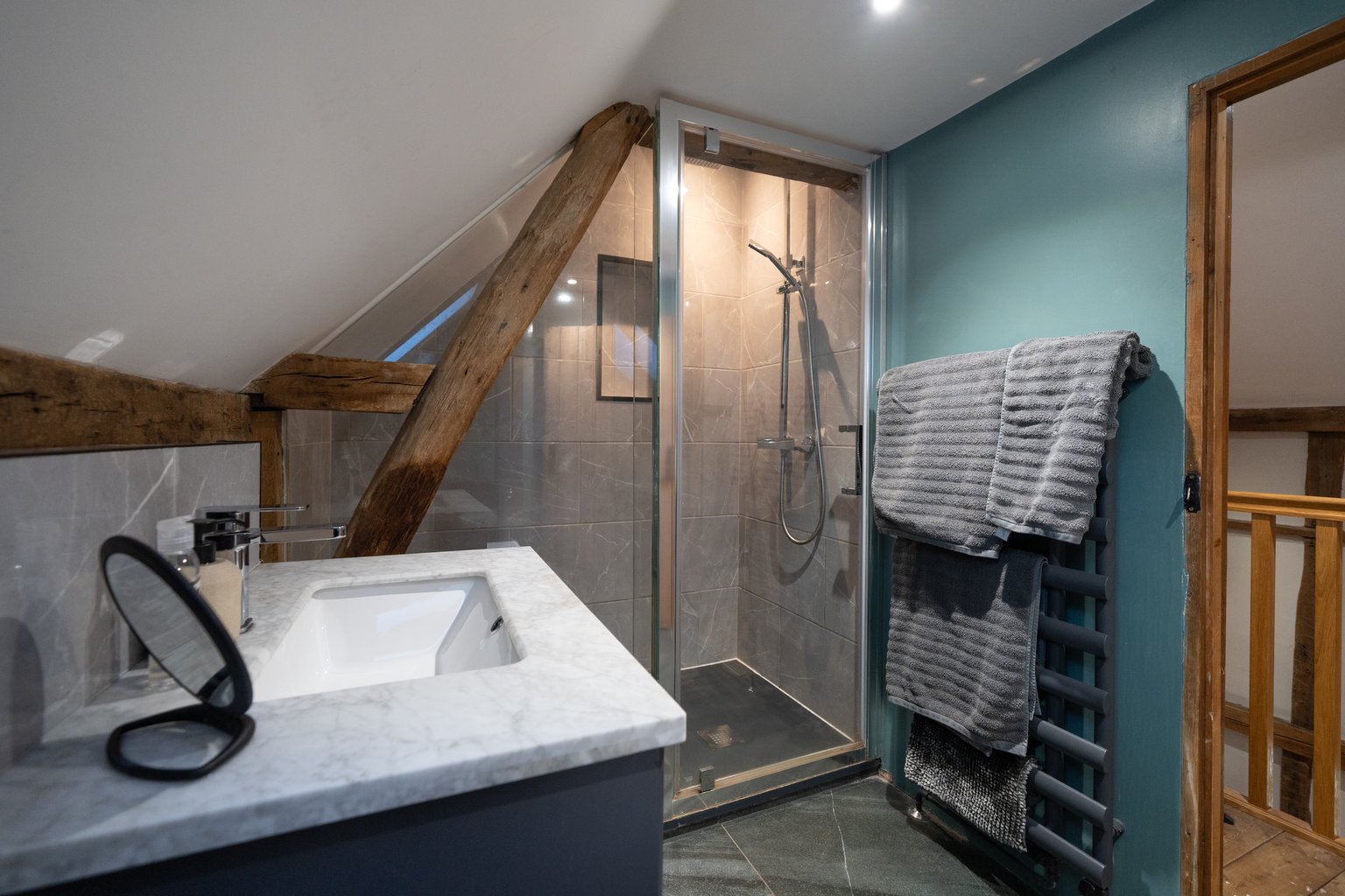 The shower room at The Oast, with a marble-topped basin, glazed walk-in shower, exposed beam and white towels on a dark towel rail