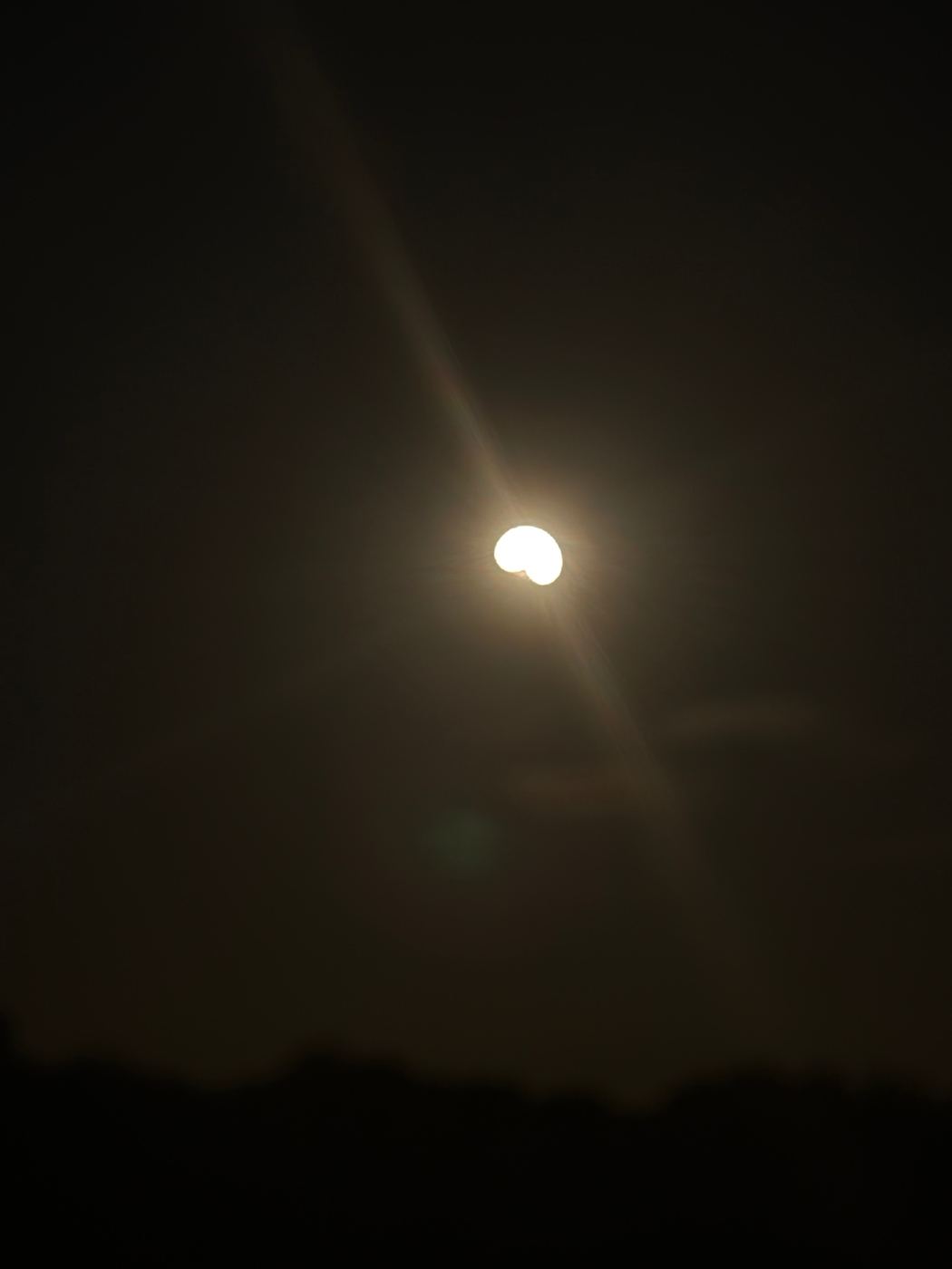 The sun photographed against a dark sky with a small bite taken out of its lower left edge as the Moon begins to cross it