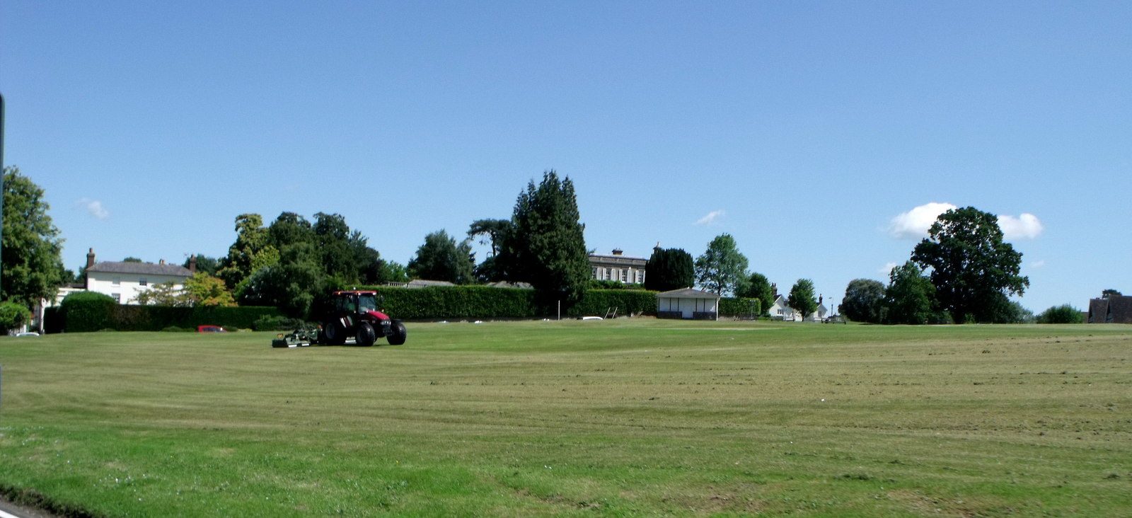 A wide view across the mown green at Frant to the tree line and rooftops of the village