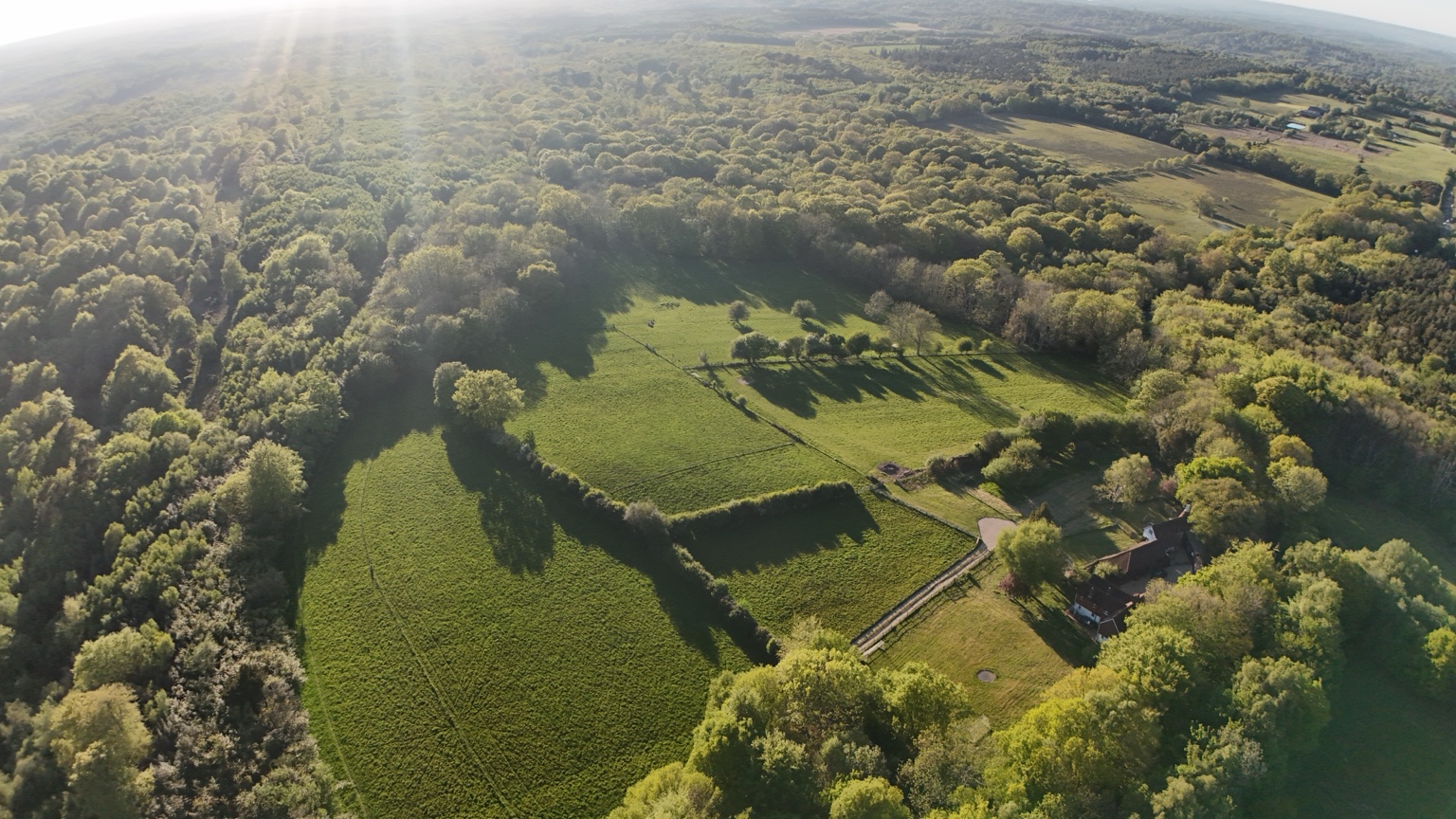 Aerial view across irregular fields, hedgerows, woodland and a scattered farmstead in the High Weald near Frant, East Sussex.