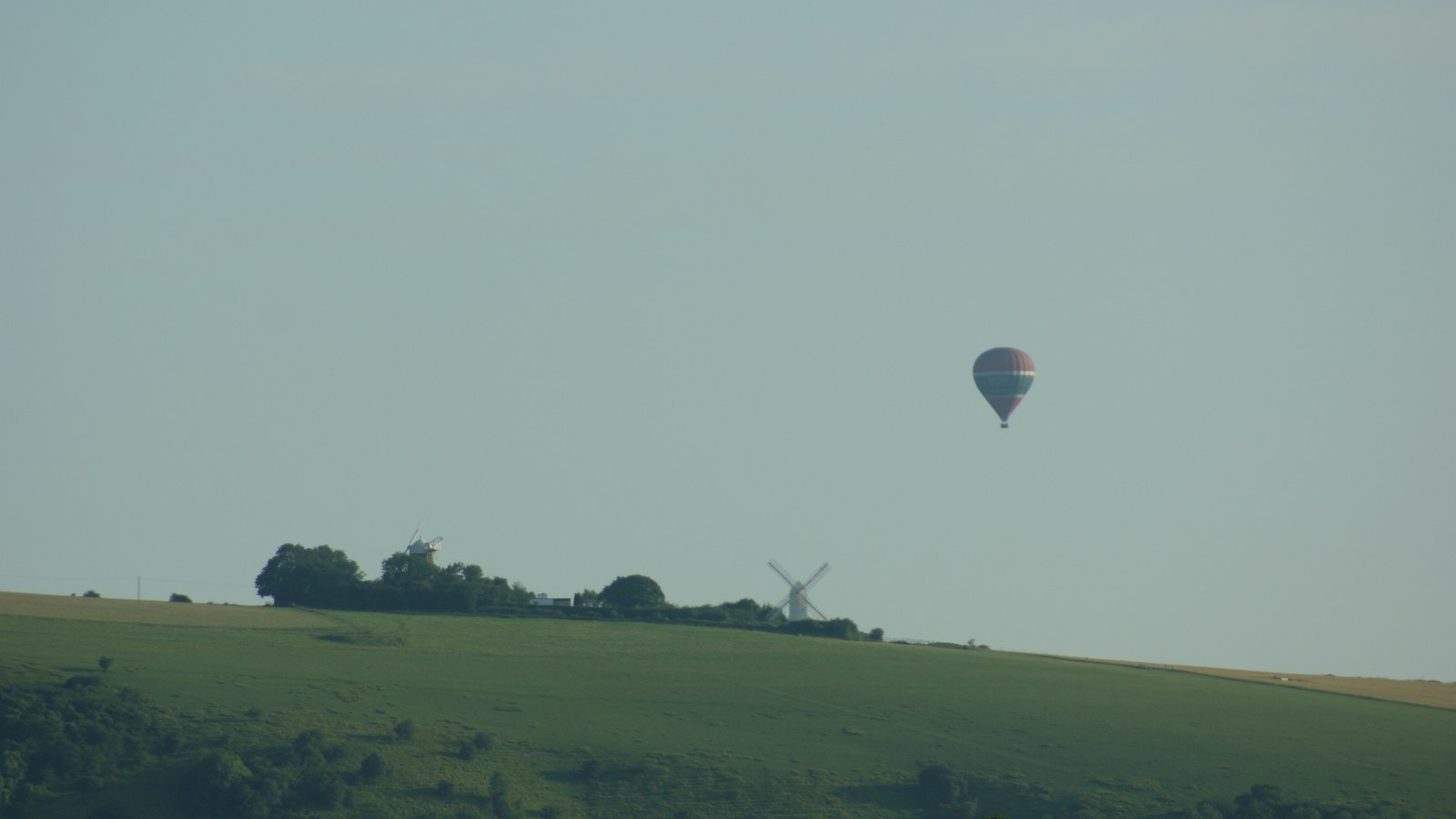 A hot-air balloon drifting low over open downland and hedged fields on the South Downs.