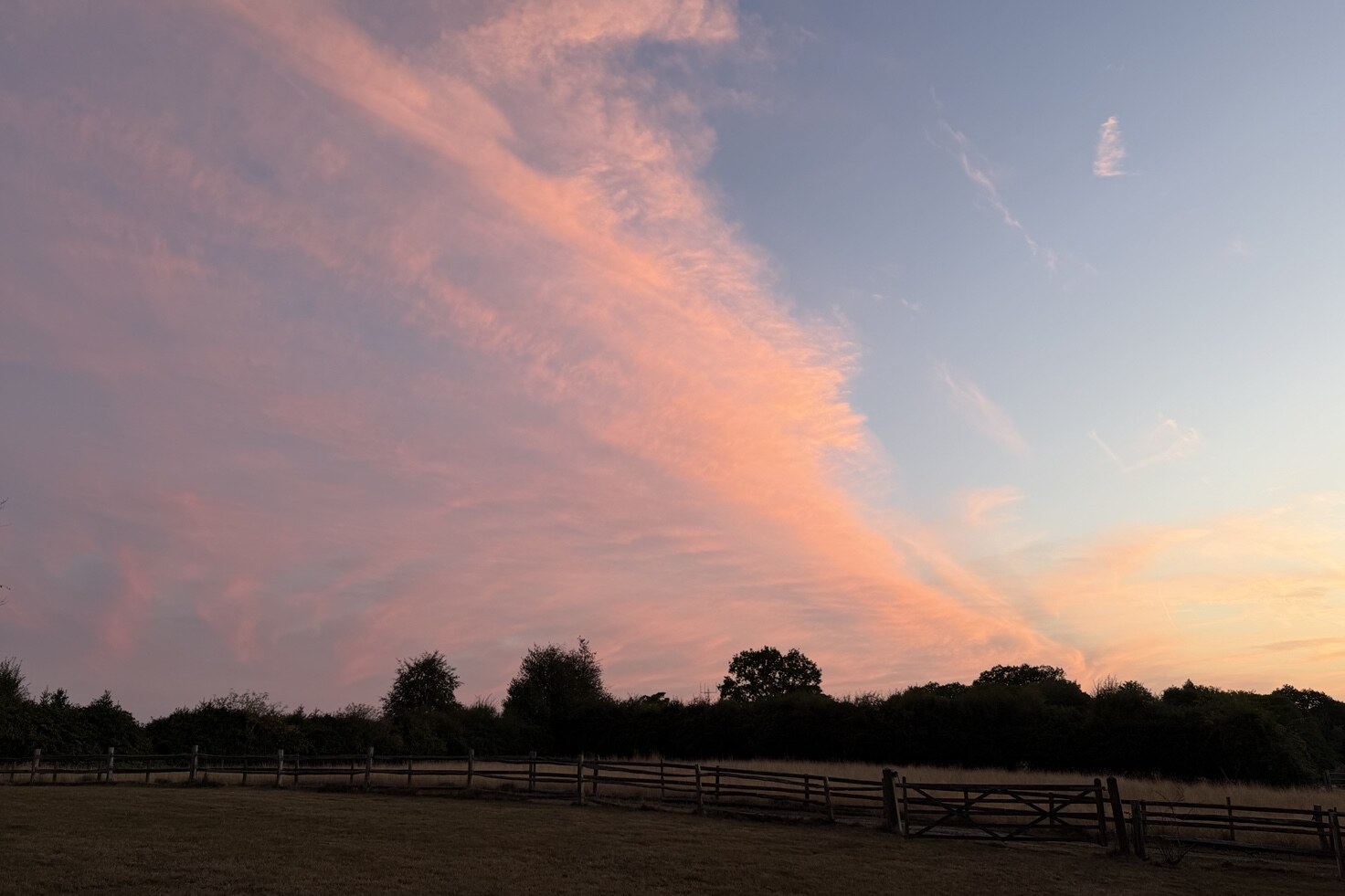 Pink sunset clouds over the paddocks and timber field gate at Martins Farm in Frant, East Sussex.