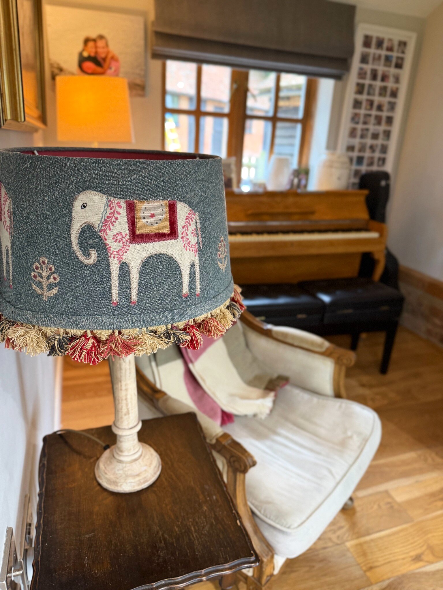 An embroidered elephant lampshade with coloured tassels at The Oast, beside a cream armchair with a pink and cream throw and the piano by the window