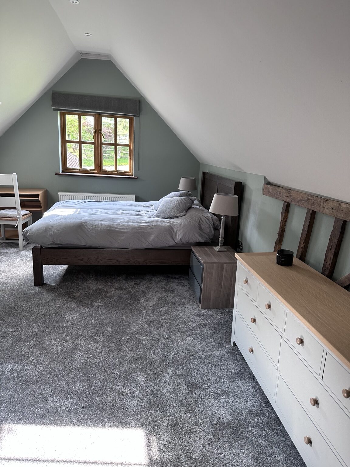 The main bedroom at The Oast, with a double bed made up in white linen beneath a sloping beamed ceiling
