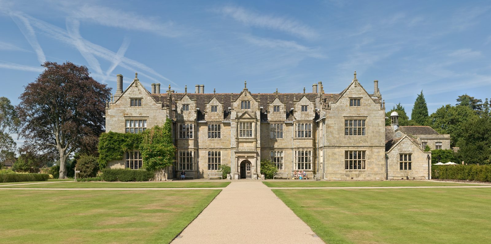 The Elizabethan stone frontage of Wakehurst Place at Ardingly, seen along a straight path across close-mown lawns under a wide summer sky